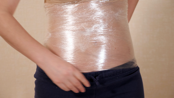 Een jonge vrouw wikkelt de taille in plastic omslag. Methode voor gewichtsverlies - Video