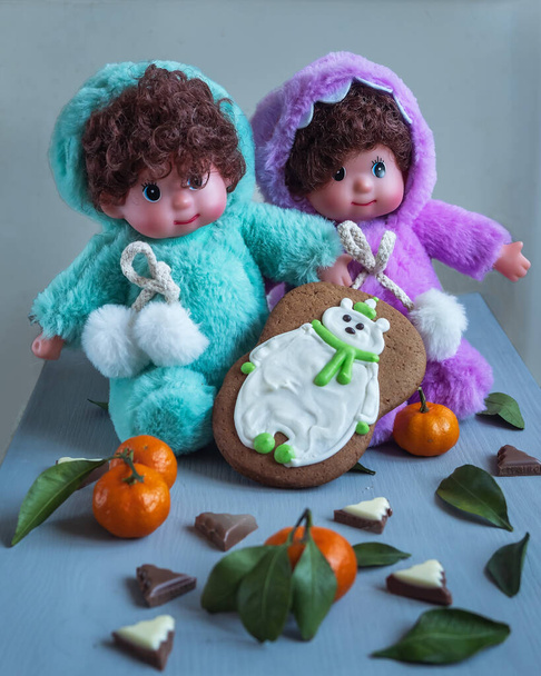 Karta okolicznościowa z bliźniaczymi lalkami w jasnych kostiumach z oszklonym piernikiem i mandarynkami - Zdjęcie, obraz
