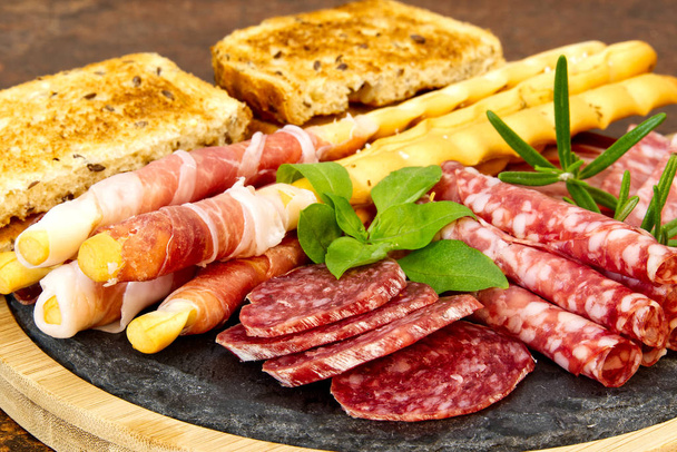 Beautiful sliced food arrangement close-up photo. Italian style antipasto plate, cheese, ham, salami, rosmarin, prosciutto - Photo, Image