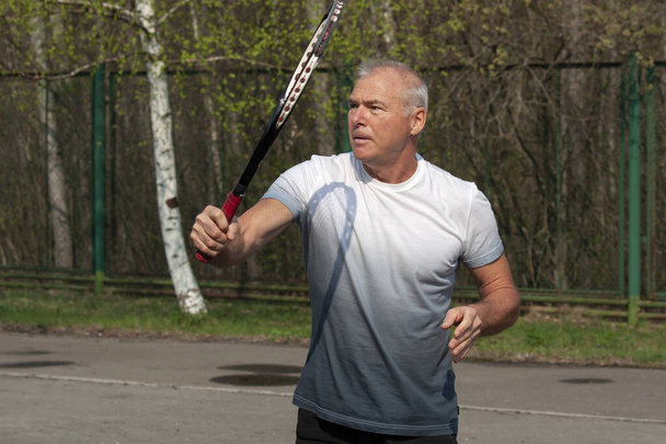 Mies pelaa tennistä ulkona kentällä
 - Valokuva, kuva