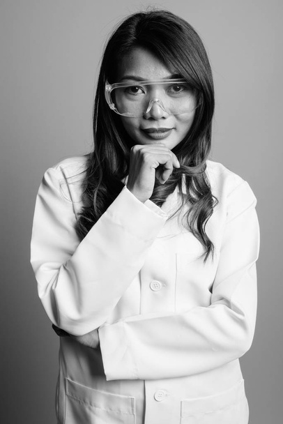 Studio shot of Asian woman doctor as scientist wearing protective glasses against gray background in black and white - Photo, image