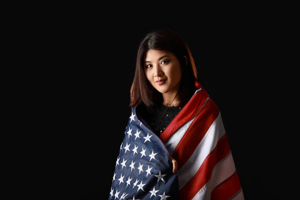 Portret van jonge Aziatische vrouw met Usa vlag op donkere achtergrond - Foto, afbeelding
