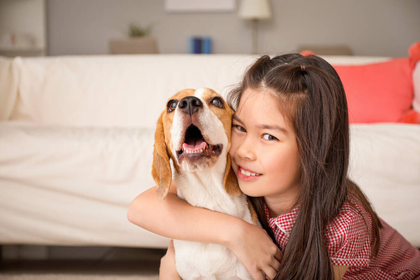 Klein Aziatisch meisje met schattig beagle hond thuis - Foto, afbeelding
