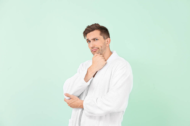 Thoughtful man in bathrobe on color background - Foto, Imagen