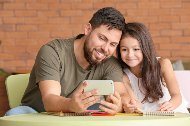 Батько і маленька дочка з мобільним телефоном вдома
 - Фото, зображення