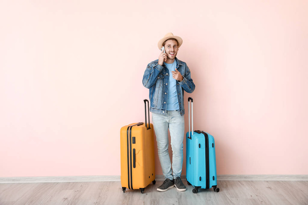 Giovane turista maschio con bagagli parlando per telefono vicino alla parete a colori
 - Foto, immagini