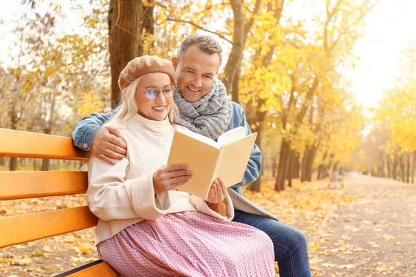 Счастливая взрослая пара читает книгу, сидя на скамейке в осеннем парке
 - Фото, изображение