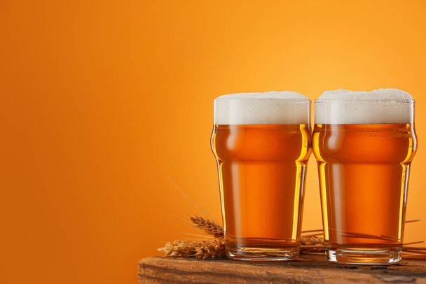 Glasses of beer on table against color background - 写真・画像