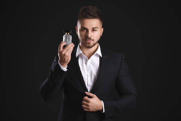 Handsome young man with bottle of perfume on dark background - Photo, image