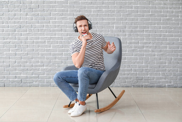 Komea mies kuuntelee musiikkia istuessaan nojatuolissa lähellä harmaata seinää
 - Valokuva, kuva