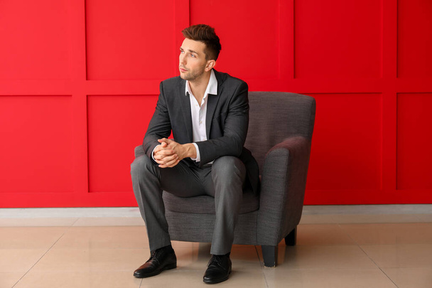Όμορφος επιχειρηματίας κάθεται στην πολυθρόνα κοντά στον τοίχο χρώμα - Φωτογραφία, εικόνα