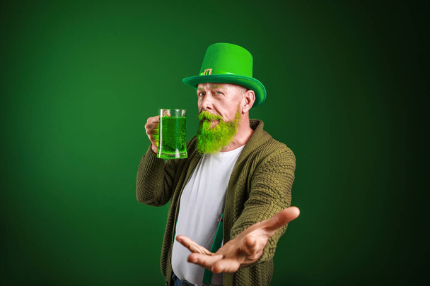 Funny mature man with glass of beer inviting viewer on dark background. St. Patrick's Day celebration - Photo, Image