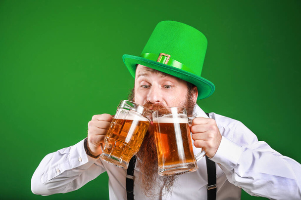 Hombre barbudo con vasos de cerveza sobre fondo de color. Celebración del Día de San Patricio
 - Foto, imagen
