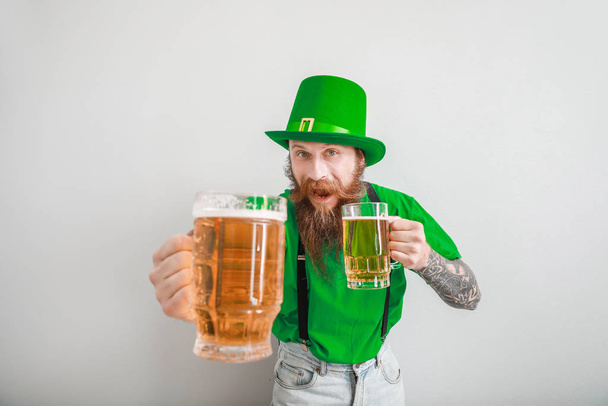 Een man met een baard en een glas bier op een lichte achtergrond. St. Patrick 's Day viering - Foto, afbeelding