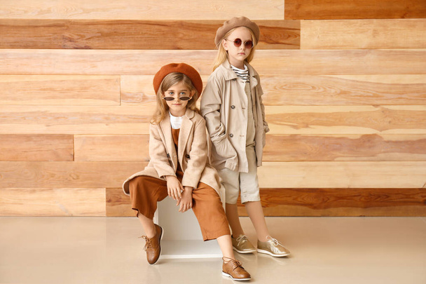 Cute little girls in autumn clothes near wooden wall - Photo, image
