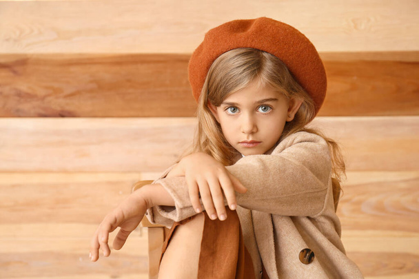 Cute little girl in autumn clothes sitting near wooden wall - Фото, зображення