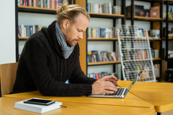 Mladý pohledný muž práce s počítačem v knihovně, muž s notebookem vnitřní použití internetu  - Fotografie, Obrázek