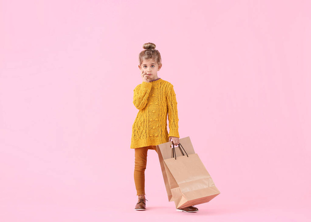 Cute little girl in autumn clothes and with shopping bags on color background - Фото, зображення
