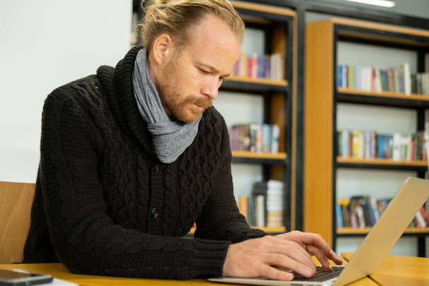 Mladý pohledný muž práce s počítačem v knihovně, muž s notebookem vnitřní použití internetu  - Fotografie, Obrázek
