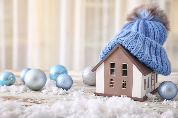 Model of house with hat and Christmas balls on table. Winter concept - Photo, Image