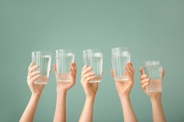 Vrouwelijke handen met glazen water op kleur achtergrond - Foto, afbeelding