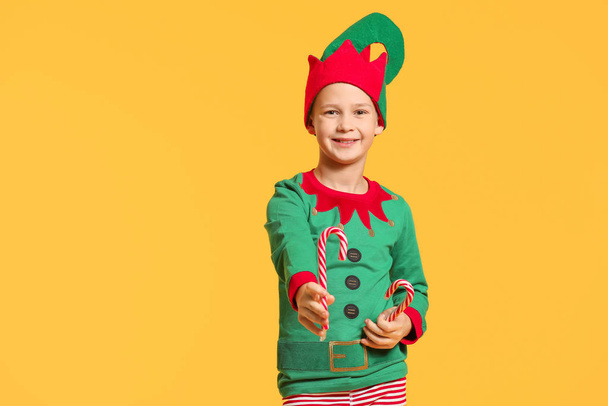Little boy in costume of elf and with candy canes on color background - Photo, Image