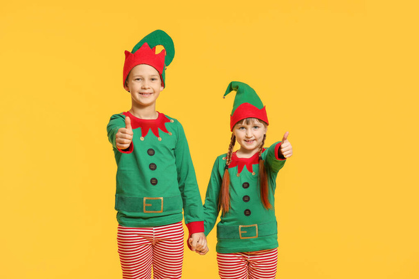 Little children in costume of elf showing thumb-up gesture on color background - Photo, Image