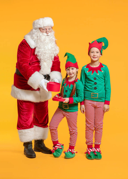 Santa Claus and little elf kids with gift on color background - Photo, Image