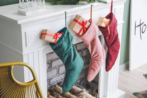 Christmas socks with gifts hanging on fireplace in room - Фото, изображение