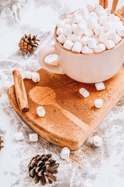a cup of Christmas New Year delicious hot chocolate and cocoa with marshmallows sprinkled with cocoa powder, cones and croissants, cinnamon on a gray table, selective focus - Photo, Image