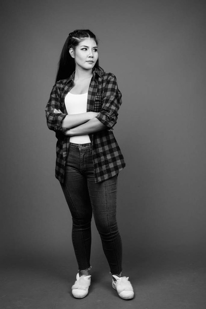 Studio shot of young beautiful Asian hipster woman against gray background in black and white - Фото, зображення