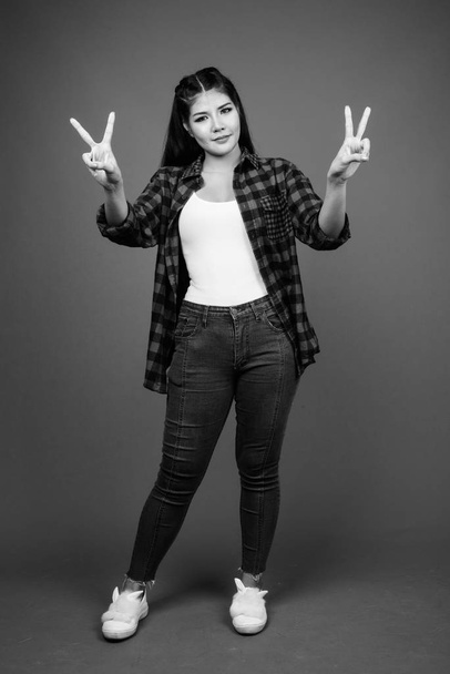 Studio shot of young beautiful Asian hipster woman against gray background in black and white - Foto, Imagem