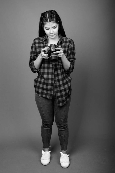 Studio shot of young beautiful Asian hipster woman against gray background in black and white - Foto, Imagen