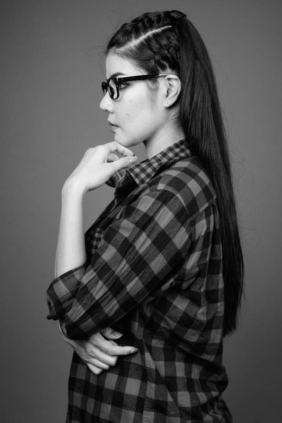 Studio shot of young beautiful Asian hipster woman against gray background in black and white - Valokuva, kuva