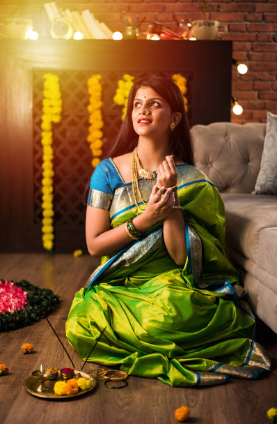 Indická dívka / ženy drží Pooja Thali při nošení zeleného saree a sedí doma s květinami rangoli a Samai, slaví Diwali nebo hinduistický festival. selektivní zaměření - Fotografie, Obrázek