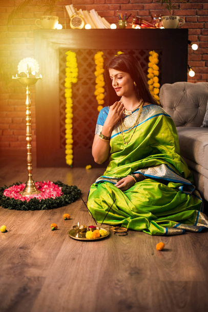 インドの少女/女性は緑のサリーを着ている間にポジャ・タイを保持し、花のランゴリーとサマイと家に座って、ディワリやヒンドゥ祭りを祝います。選択的焦点 - 写真・画像