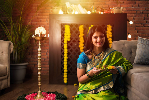 Indiai lány / nők kezében Pooja Thali, miközben zöld szárit visel, és otthon ül a virág rangoli és Samai, ünnepli Diwali vagy hindu fesztivál. szelektív fókusz - Fotó, kép