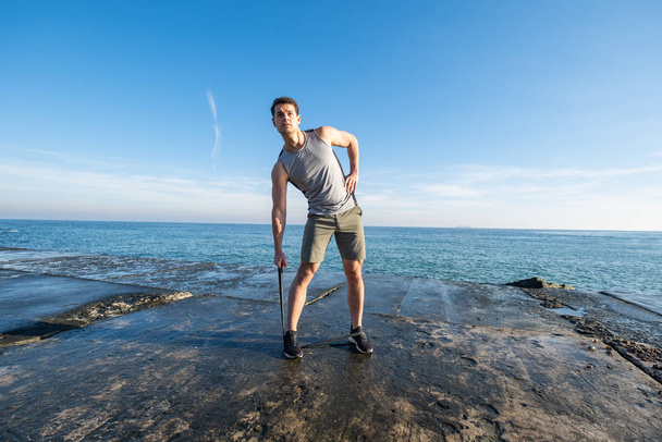 Young fit male training with  athletic rubber on the beach in summer day - Fotó, kép