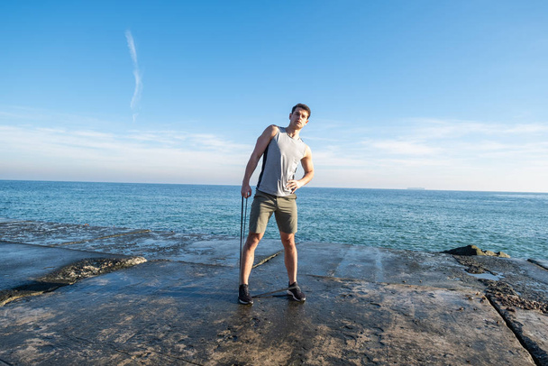 Young fit męski trening z gumą atletyczną na plaży w letni dzień - Zdjęcie, obraz