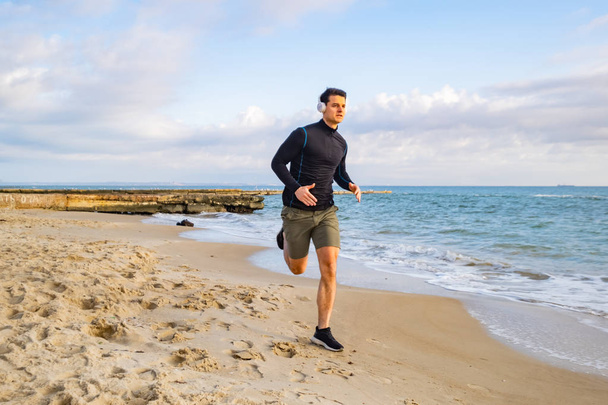 Fit male runner training on the summer beach and listen to music against beautidul sky and sea - Foto, Imagem