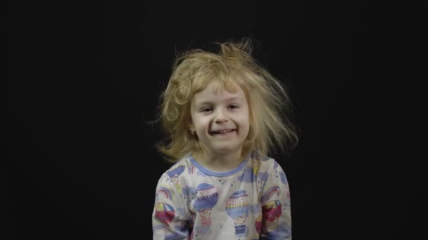 Het kleine meisje in pyjama loopt rond en trekt gezichten. Zwarte achtergrond - Video