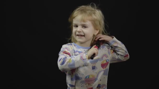 kleines Mädchen im Pyjama mit lustigem Kopfschmuck kämmt. schwarzer Hintergrund - Filmmaterial, Video