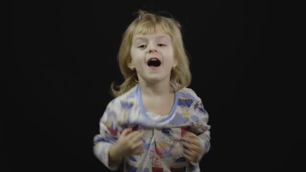 Het kleine meisje in pyjama loopt rond en trekt gezichten. Zwarte achtergrond - Video