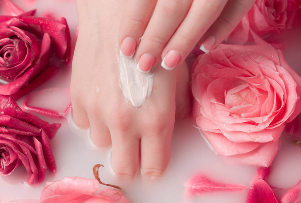 Spa Salon: Mooie vrouwelijke handen met Franse Manicure in de schaal van het water met roze rozen en rozenblaadjes. - Foto, afbeelding