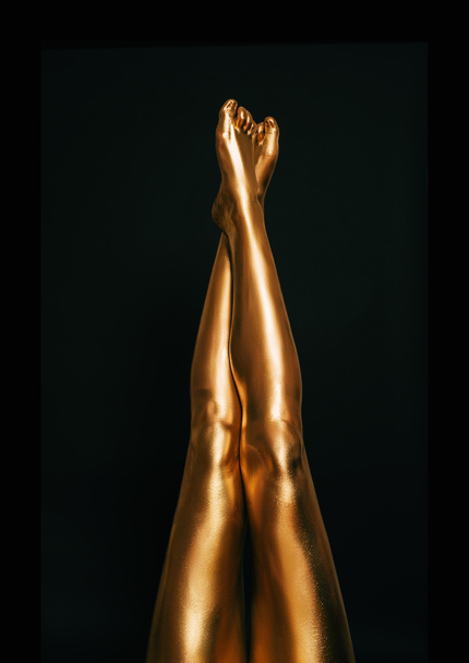 美しいと洗練された女性の足は、黒の背景、美しさとファッションのコンセプトにポーズを黄金の塗料で覆われて - 写真・画像