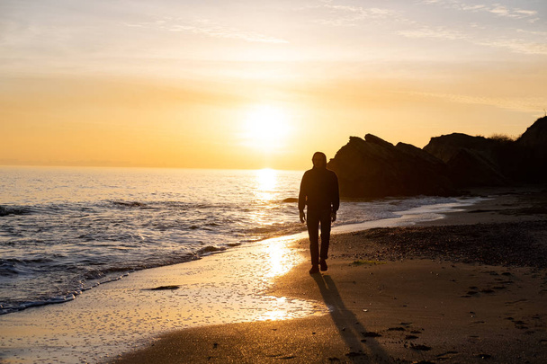sziluett férfi utazó állni sziklák közelében, és nézni gyönyörű naplemente a tengerben - Fotó, kép