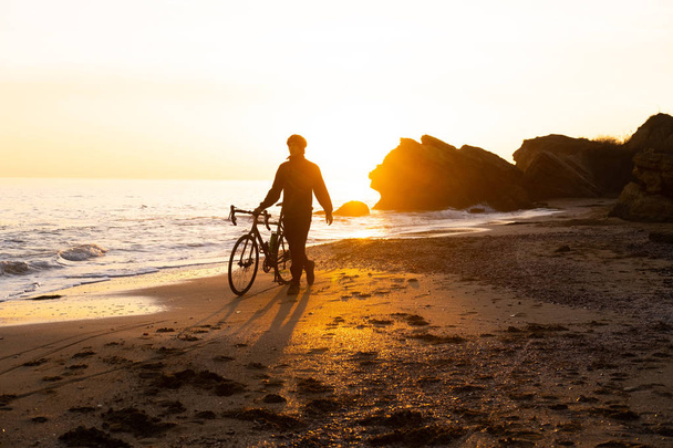 Silhouette eines jungen männlichen Fahrradfahrers mit Helm am Strand bei schönem Sonnenuntergang - Foto, Bild