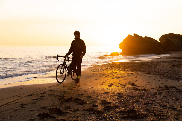 sziluett fiatal férfi kerékpáros bukósisakban a strandon alatt gyönyörű naplemente - Fotó, kép