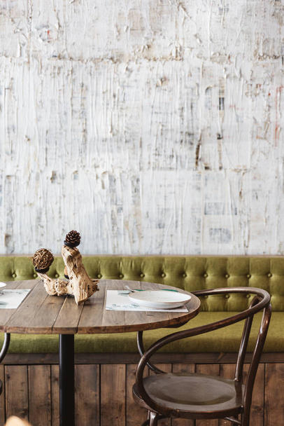 Yemek salonu yeşil kanepe, ahşap masa, siyah çelik sandalye ve beyaz çizik desenli duvar kağıdı ile süslenmiş. Modern restoran atmosferi. - Fotoğraf, Görsel