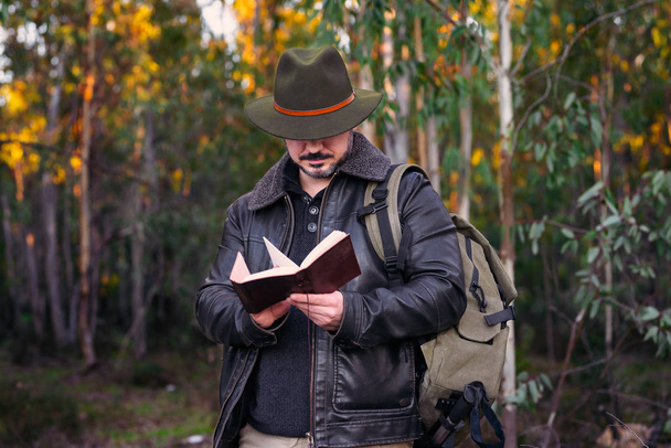 Ώριμος άνδρας με καπέλο και σακάκι αναζητούν παλιό βιβλίο για το δάσος με c - Φωτογραφία, εικόνα